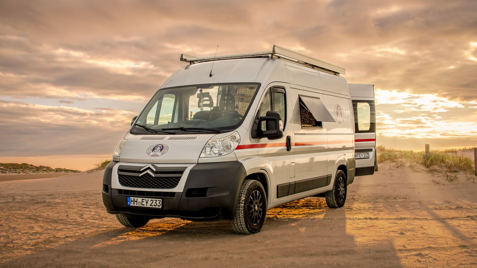 Arty Vans Jumper Camper in Totale von vorne rechts am Strand im Sonnenuntergang