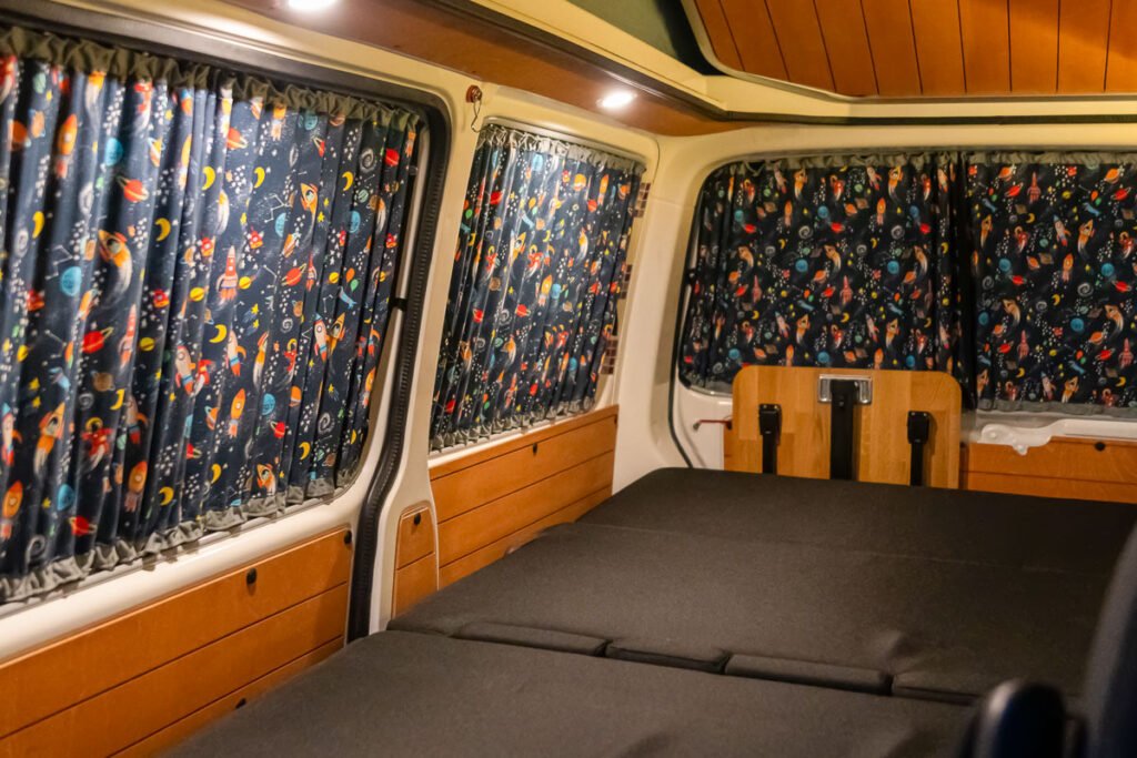 Arty Vans Creations VW T6 Camper Innenraum. - Zum Bett umgeklappte Schlafsitzbank und zugezogenen Premium-Design-Vorhänge mit Weltraummuster.
