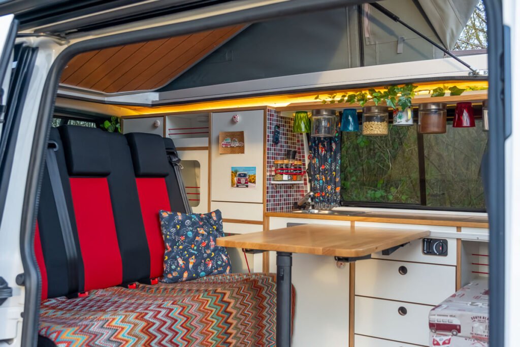Arty Vans Creations VW T6 Bulli Innenraum mit Blick durch die Schiebetür. Eichenholz, warme Farben, Designvorhänge usw.
