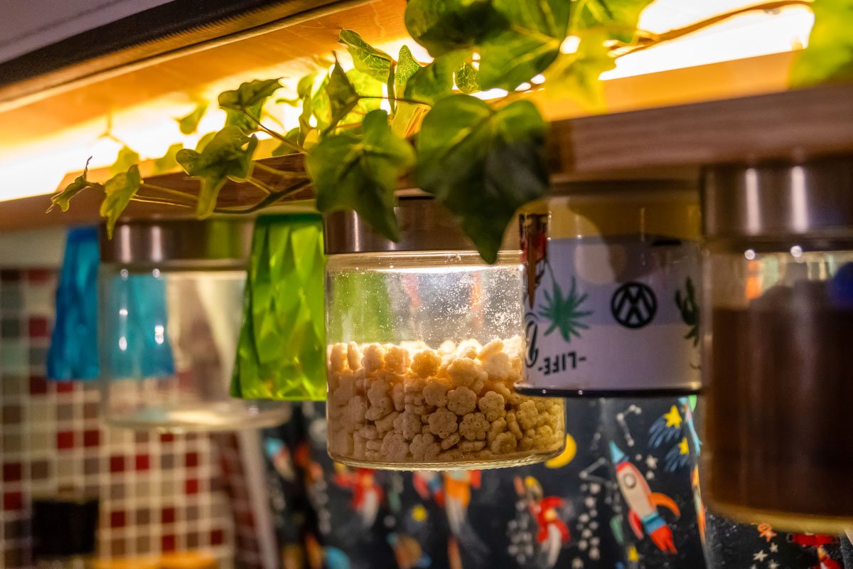 Arty Vans Creations VW T6 Camper Innenraum. - Detail des Küchenboards mit Gläsern, Emailletassen, Pflanzen, Designvorhängen usw.