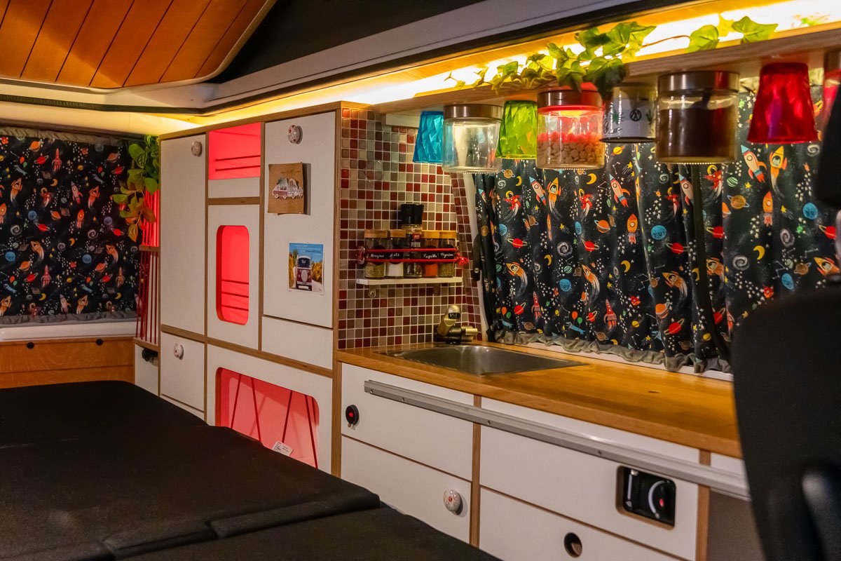 Arty Vans Creations VW T6 Camper Innenraum. - Küchenzeile mit Eichenholz, warmen Farben, 3D-Fliesen, Gläser, Designvorhängen usw.