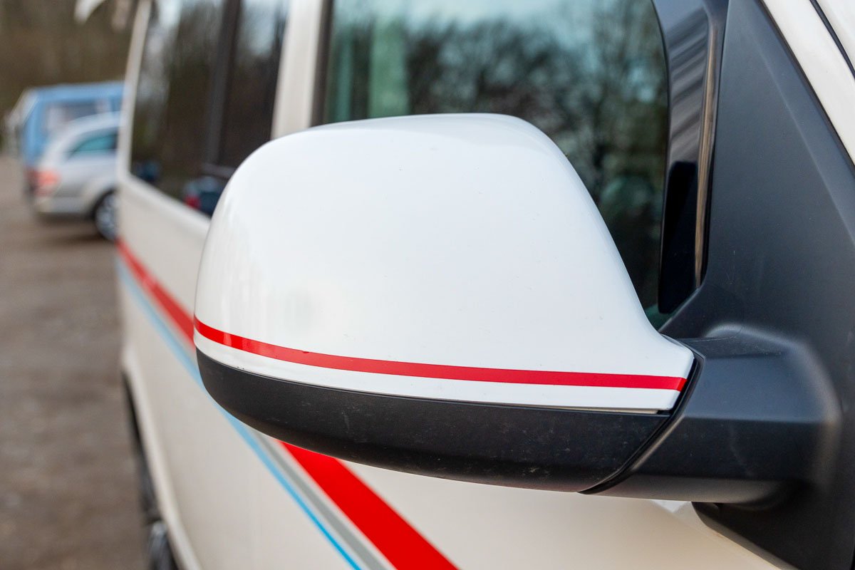 Arty Vans Creations VW T6 Bulli mit auf einem Schotterweg in der Natur - Detail weiße Bulli Seitenspiegelkappen